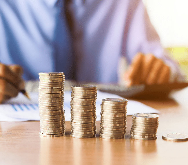Stacks of coins increasing in height with a blurred person in the background.