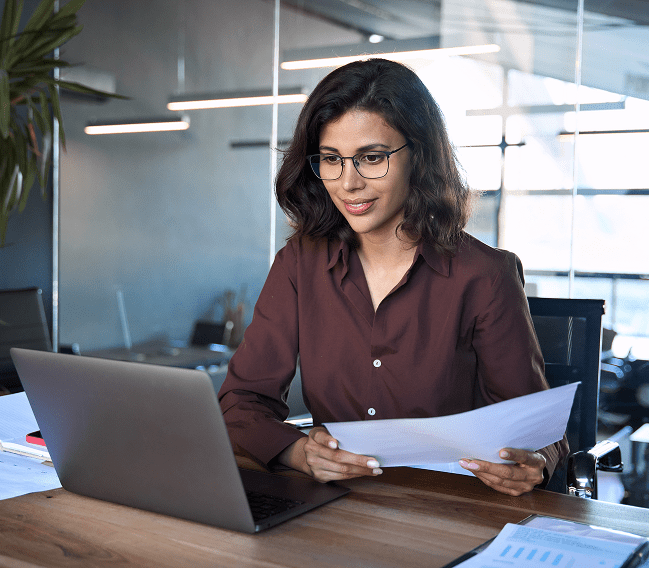 Woman working on laptop with documents in modern office.